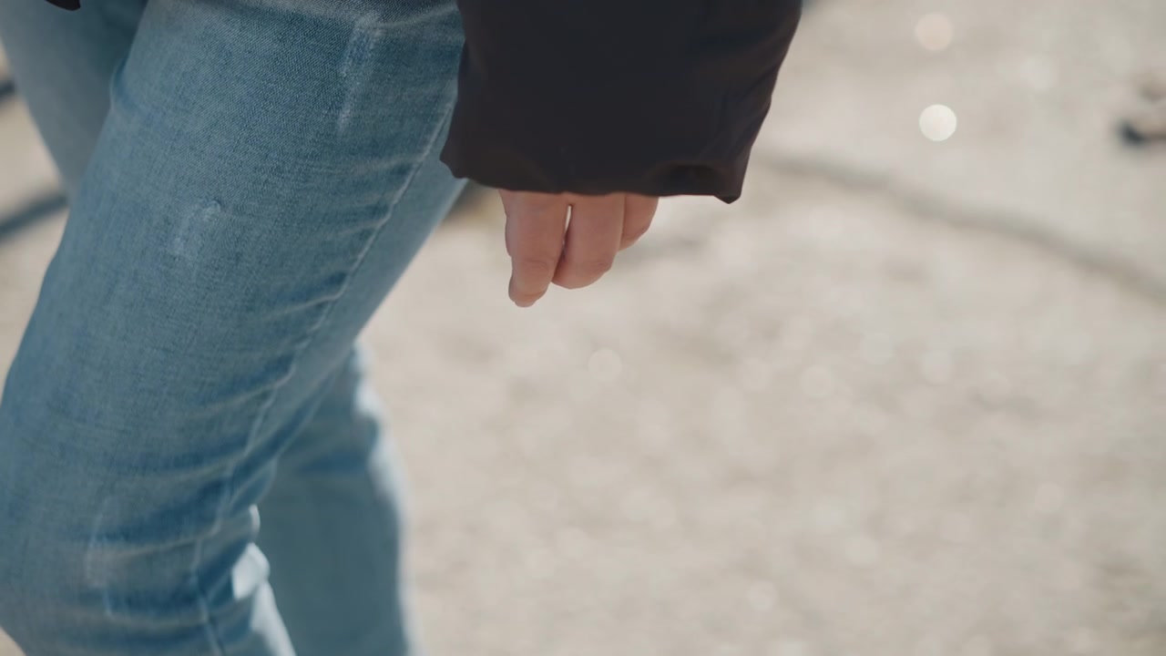 Woman walks outdoors wearing black jacket and blue jeans. focus remains on her lower body as woman moves along paved path with natural light casting shadows from nearby objects