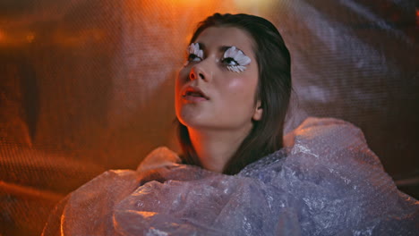 imaginative makeup woman posing in bubble wrap with petal eyelashes closeup.