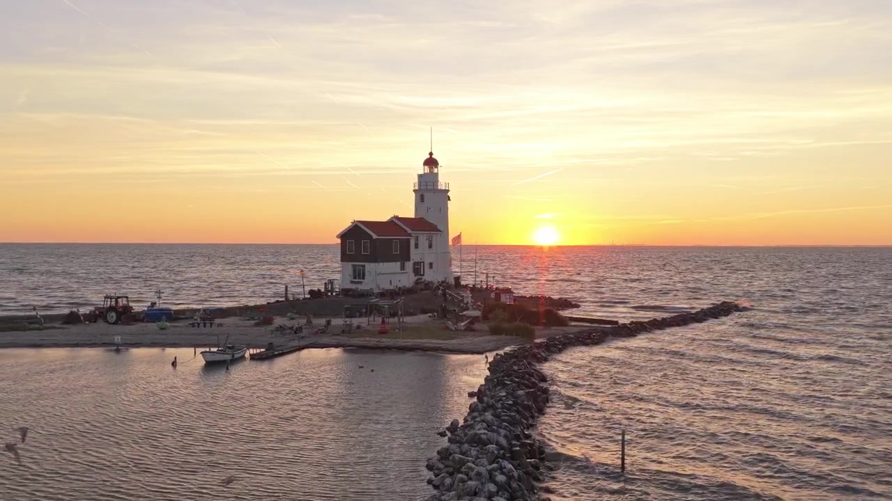 Sole dorato che tramonta sul mare calmo accanto allo storico faro Paard van Marken. Turisti che ammirano l'iconico punto di riferimento olandese in Olanda.