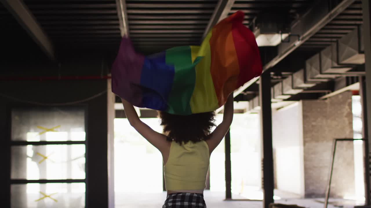 Mixed race woman holding rainbow flag running through an empty building