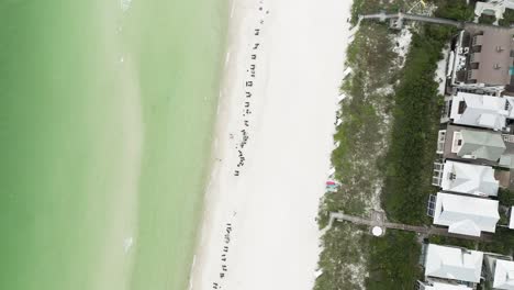 Geradeaus-Langsamer-Spin-Bewegung-Nach-Unten-Und-Blick-Auf-Den-Rosigen-Strand-Mit-Wellenbewegung,-Liegestuhl-Auf-Sand,-Büschen-Und-Einigen-Häusern