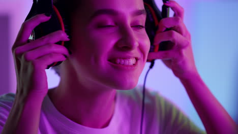 Cyber-girl-put-headphones-in-pink-neon-lights-closeup.-Smiling-esport-gamer