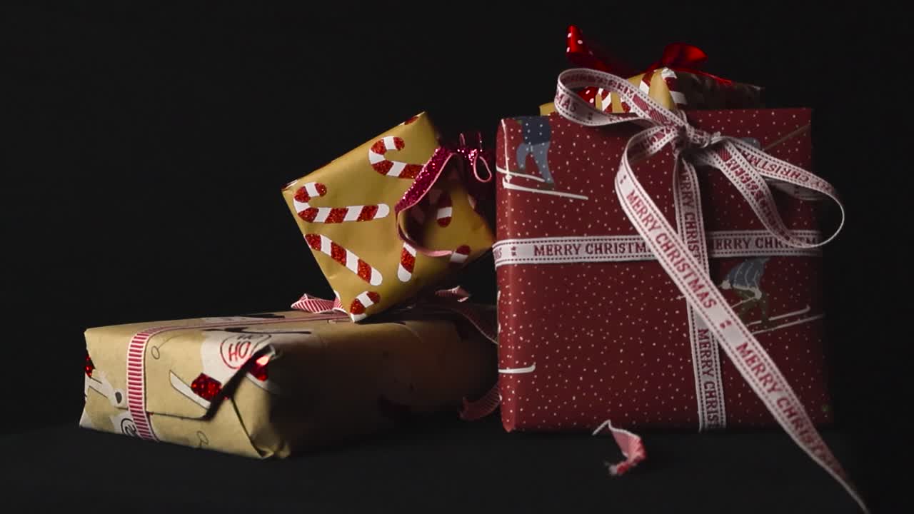 Gorgeous wrapped and packed Christmas holiday presents placed in front of a black studio background with colorful packaging and ribbons. Candy canes and Merry Christmas text visible on presents