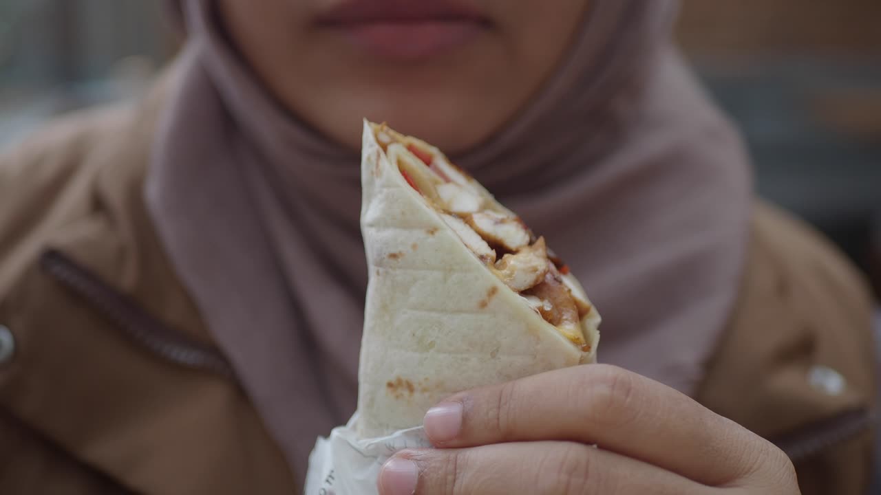 una mujer con hijab come un envoltorio de pollo