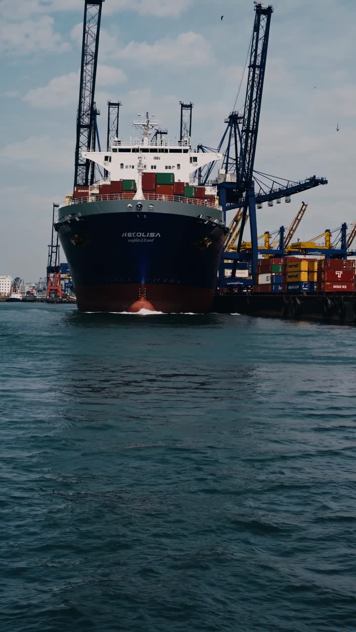 Dynamic low-angle video shot of a large cargo ship docked at a bustling port, emphasizing the ship's