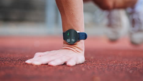 athletic man training on red running track with smartwatch display tracking ecg, heart rate and training progress