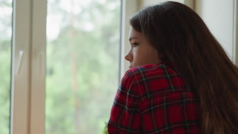 una mujer joven mira por una ventana pensativa