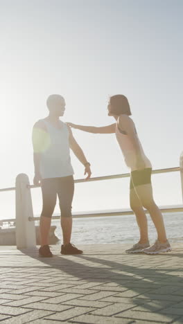 vertical video of happy biracial couple stretching on promenade, in slow motion