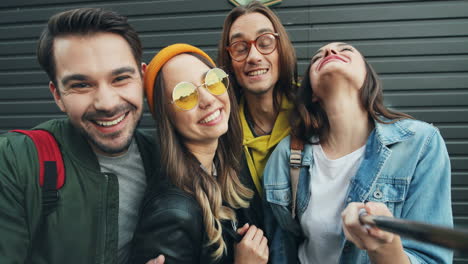 close-up view of group of caucasian funnt friends in hipster style smiling and posing while taking selfies in the street