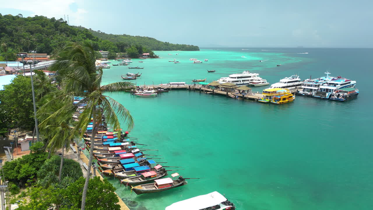 muchos barcos de pesca coloridos están amarrados cerca de la orilla, detrás de las palmeras, y los yates están amartados en el muelle