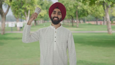 happy sikh indian man using money as fan in park