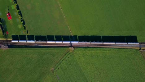 aerial view stationary train sitting on tracks in green field with shadows