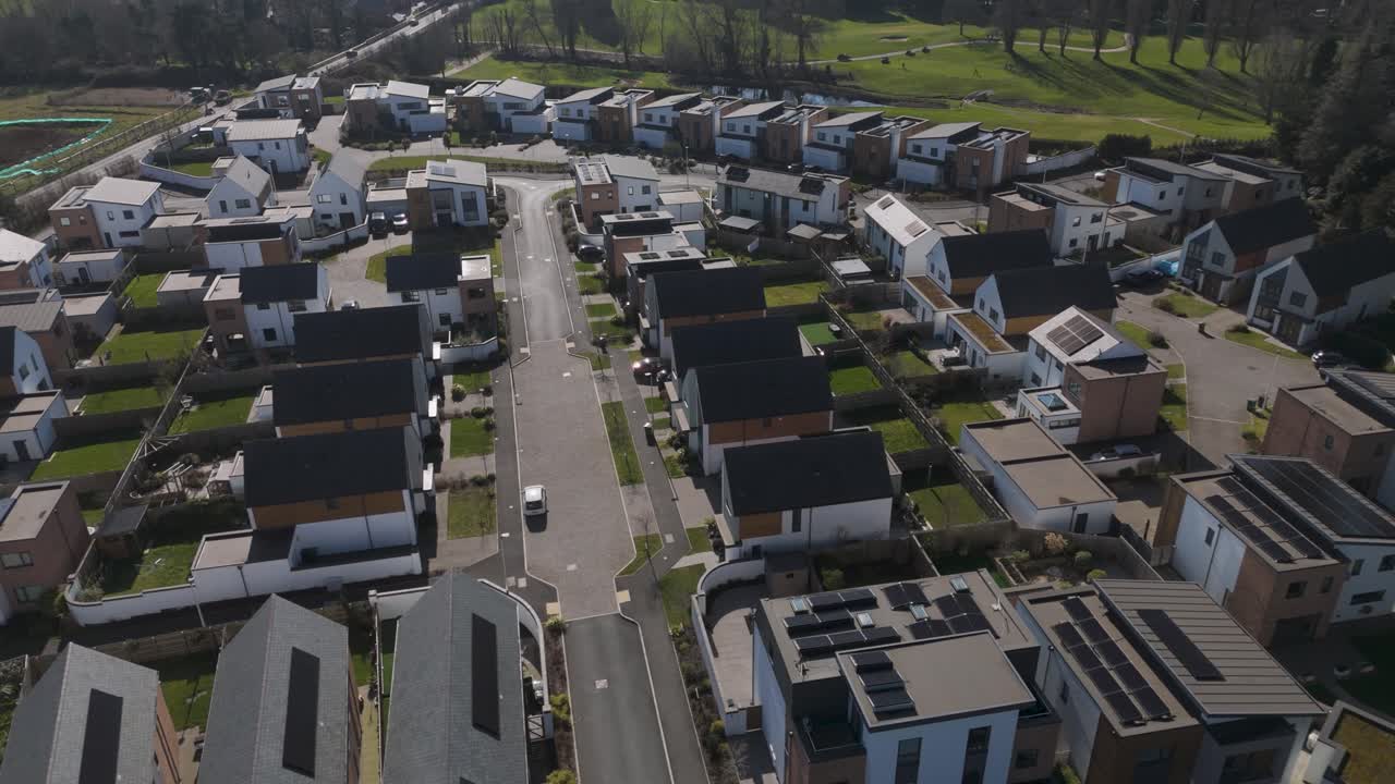 Aerial push-in over luxury modern housing estate of flat-roof solar-equipped homes, neat gardens and looping streets showcasing sustainable upscale suburban design