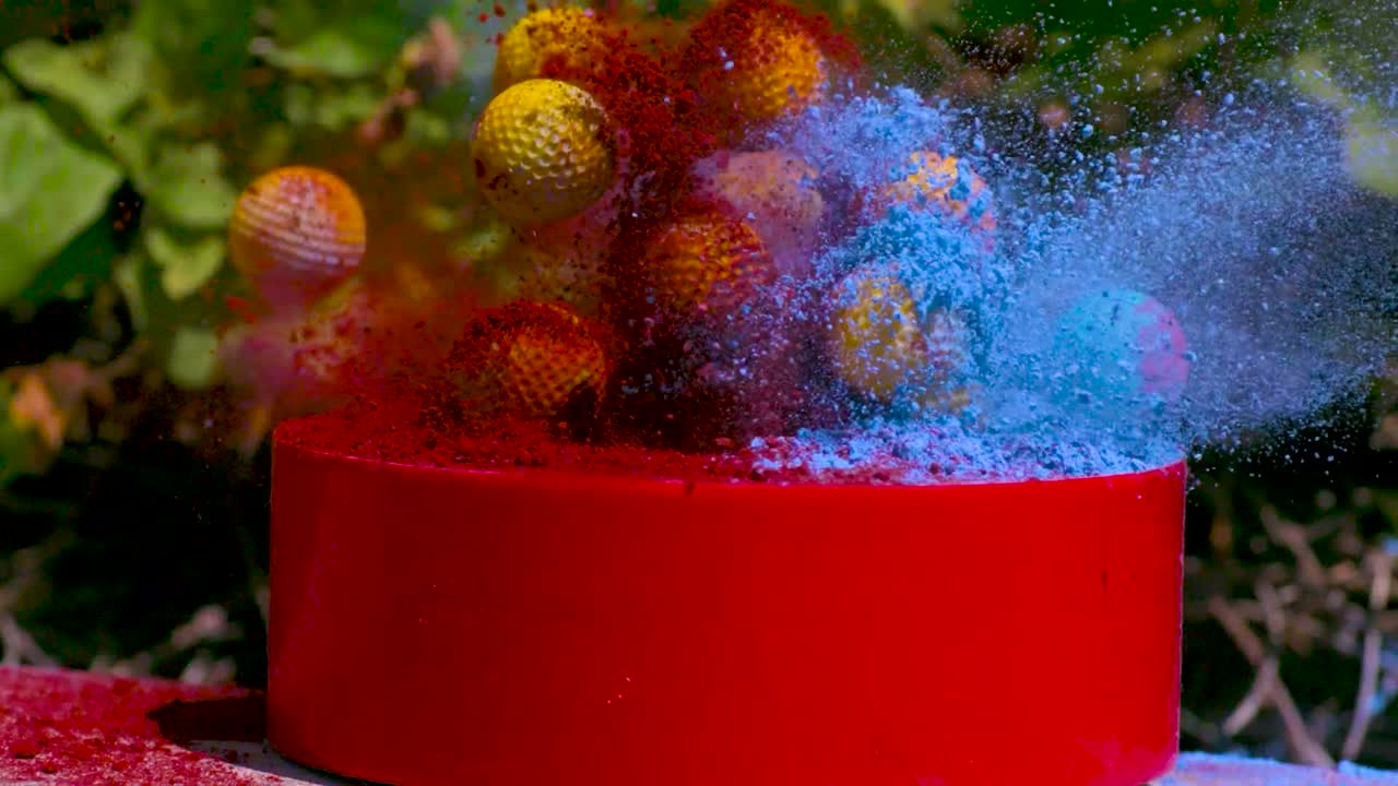 bolas amarillas con textura cubiertas con polvo de tiza azul y rojo que se lanzan con otra bola en cámara lenta