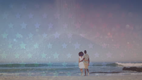 animation of stars over back of african american couple walking on beach