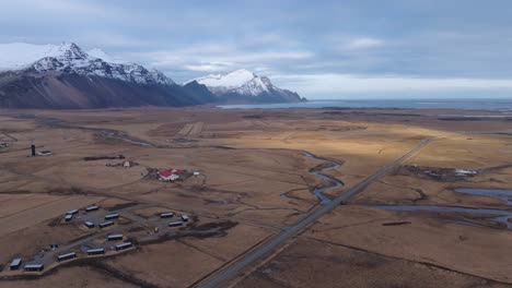 Pequeño-Pueblo-En-El-áspero-Paisaje-Islandés-Debajo-De-Montañas-Nevadas