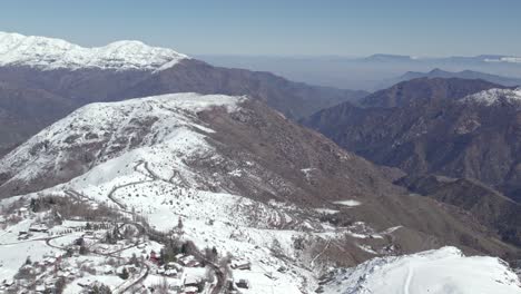 Aerial-establishing-shot-of-snow-capped-mountains-within-the-Farellones-district-pollution-in-the-Santiago-Valley