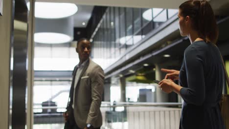 Diverse-businessman-and-businesswoman-talking,-waiting-for-lift-and-arriving-in-modern-office