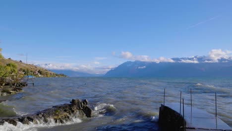 waves crashing on small port entrance and dismantled railing shores of lake léman, the alps in the background