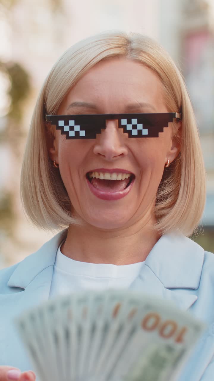 행복한 부유한 성숙한 사업가 여성은 도시 거리에서 달러 돈을 보여주는 강도 생활 선글라스를 착용합니다.