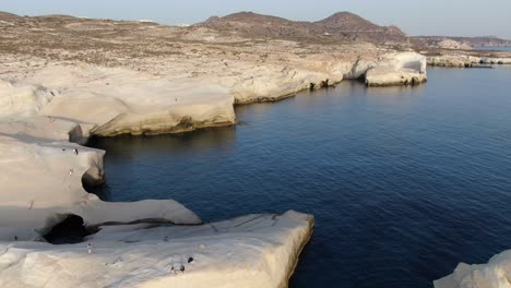 Drone-view-in-Greece-flying-over-a-moon-shaped-white-rock-area-in-Milos-island-at-sunrise-next-to-the-dark-blue-sea