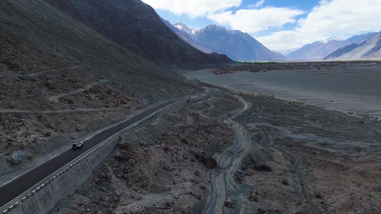 Aerial drone shot showcasing a car crossing the sandy stretches of Nubra Valley, with distant peaks framing the scene.