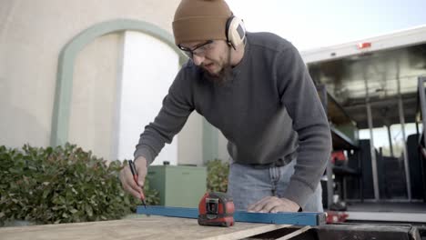 caucasian male contractor marks wood plank with straight edge or rule