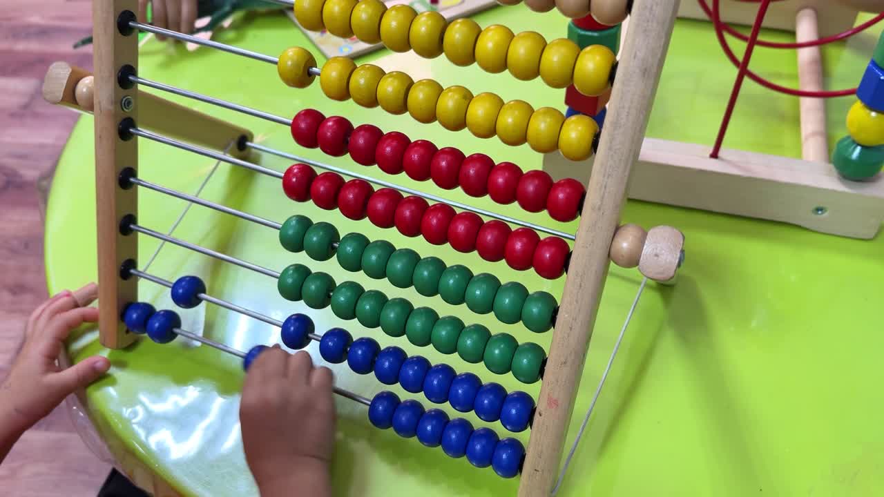 A young child interacts with a colorful abacus, learning to count and sort. Perfect for educational content, e-learning visuals, or preschool promos. Captured in crisp 4K resolution.
