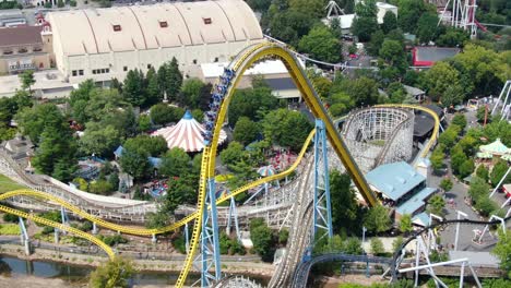 a roller coaster car of people, unrecognizable, crests the top of a roller coaster, then plunges down, aerial drone view