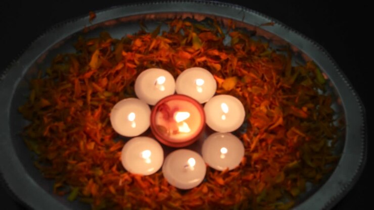 Inclinazione verso il basso su Diyas o lampade in un piatto d'argento con petali accese per Diwali, il 'Festival delle luci', importante antico festival indù celebrato per significare la vittoria della luce sull'oscurità