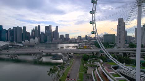 Video-Aéreo-Del-Horizonte-De-La-Ciudad-De-Singapur-Con-La-Noria-De-Observación-Del-Volante-De-Singapur,-El-Hotel-Marina-Bay-Sands-Y-Los-Jardines-Junto-A-La-Bahía-Al-Amanecer.