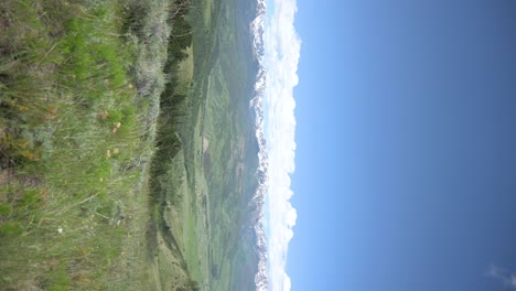 view from the top of a colorado hiking trail overlooking a green valley with snowcapped mountains, vertical