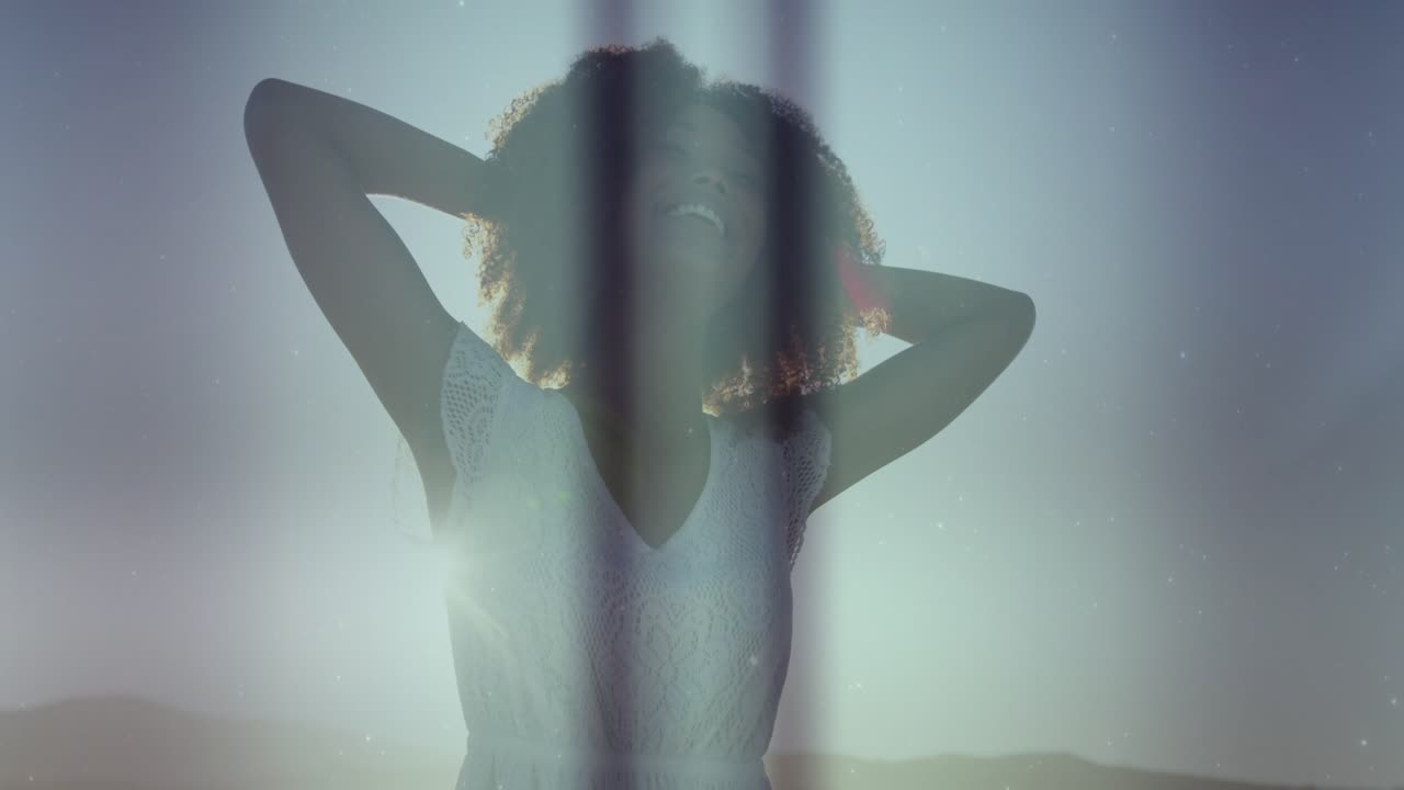 Donna in piedi, il sole crea bande di luce verticali, con le braccia dietro la testa, sorridente per scopi di branding.
