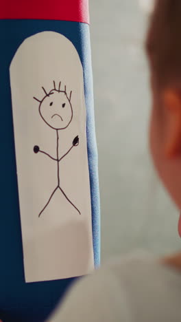 schoolgirl draws upset man on punching bag in playing room close rare view. little girl visualizes anger feeling to deal with offence in home gym