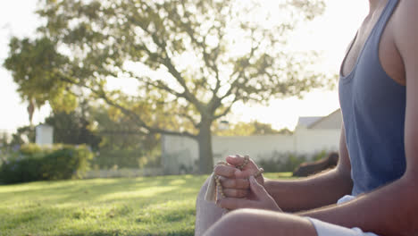 Hombre-Birracial-Enfocado-Practicando-Meditación-De-Yoga-En-Un-Jardín-Soleado,-Cámara-Lenta