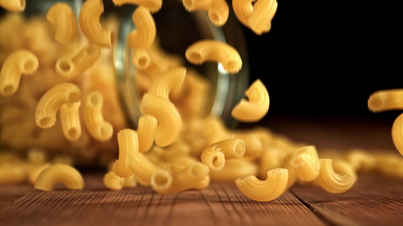 Maccheroni secchi che cadono su un tavolo di legno al rallentatore