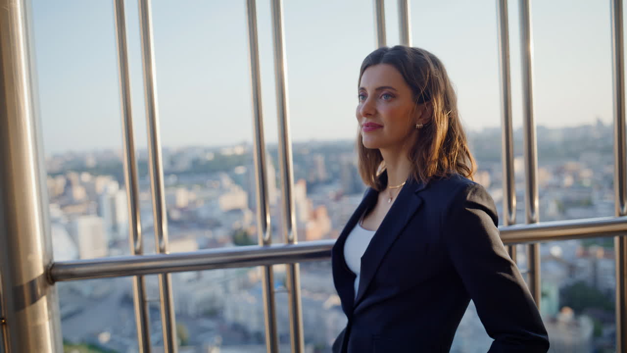 Close-up de uma mulher bem-sucedida em pé na sacada de um prédio alto, apreciando a vista da cidade
