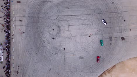 vista aérea de drones de tres automóviles de rendimiento modificado rápidos y furiosos coches de deriva quemando el evento de carrera quemando goma en el asfalto del estacionamiento de la pista de video con los transeúntes