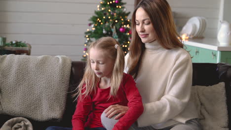 madre e hija sentadas en el sofá de la sala de estar con adornos navideños