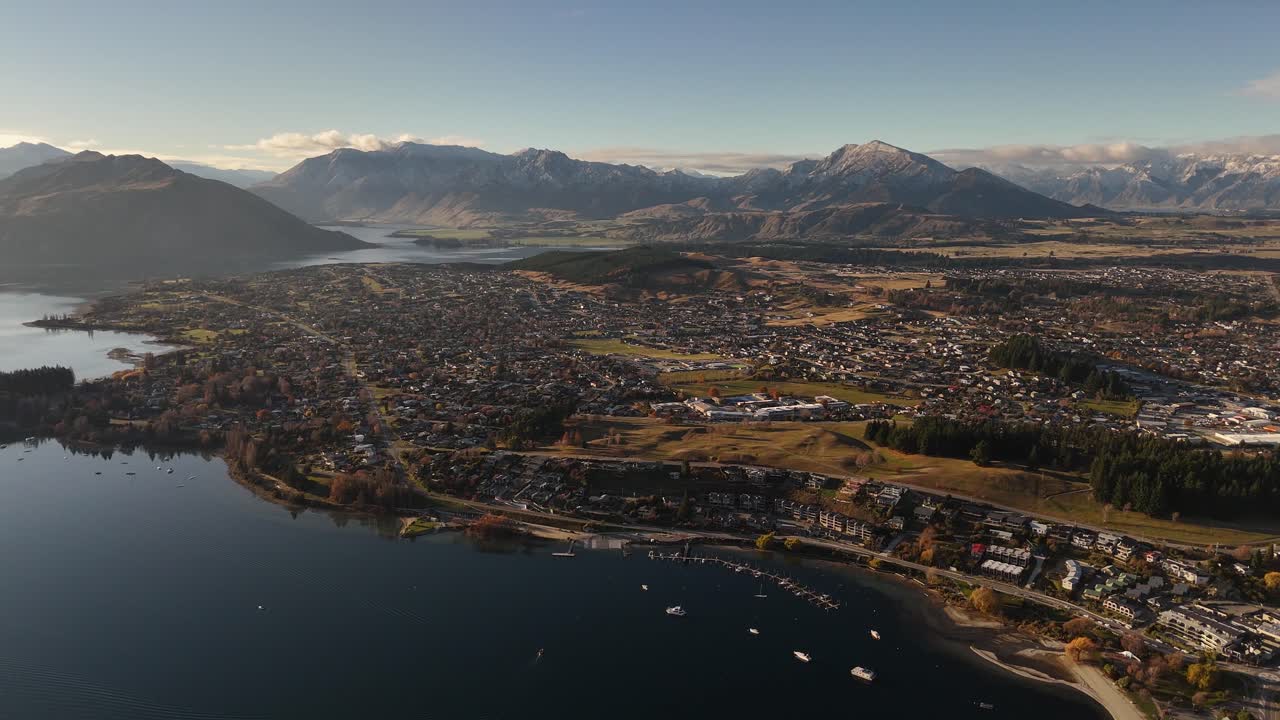 Ripresa aerea in retromarcia sul lago Wanaka che rivela la città, il porto e le montagne durante una splendida ora d'oro al tramonto, Nuova Zelanda