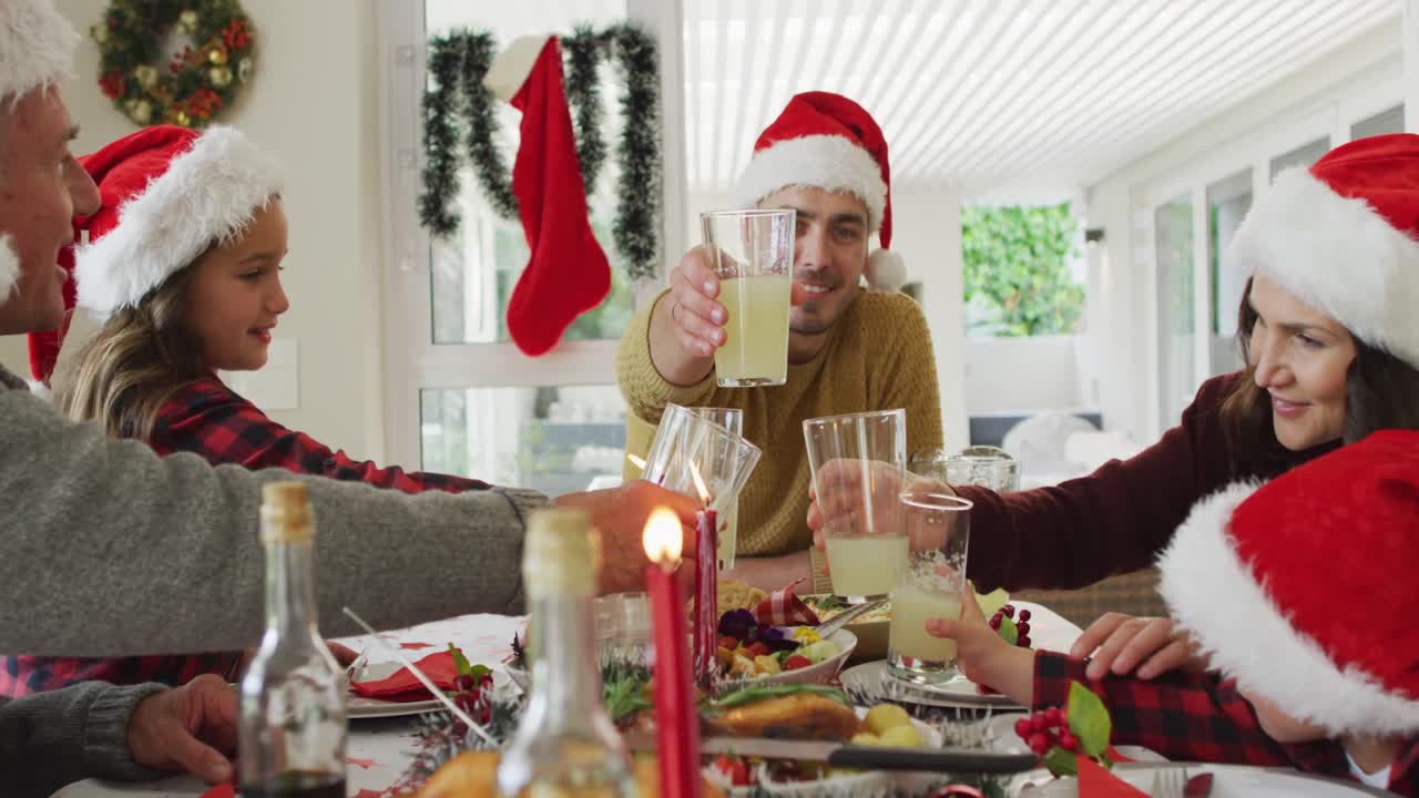 familia caucásica feliz de varias generaciones con sombreros de papá noel, teniendo la comida de navidad