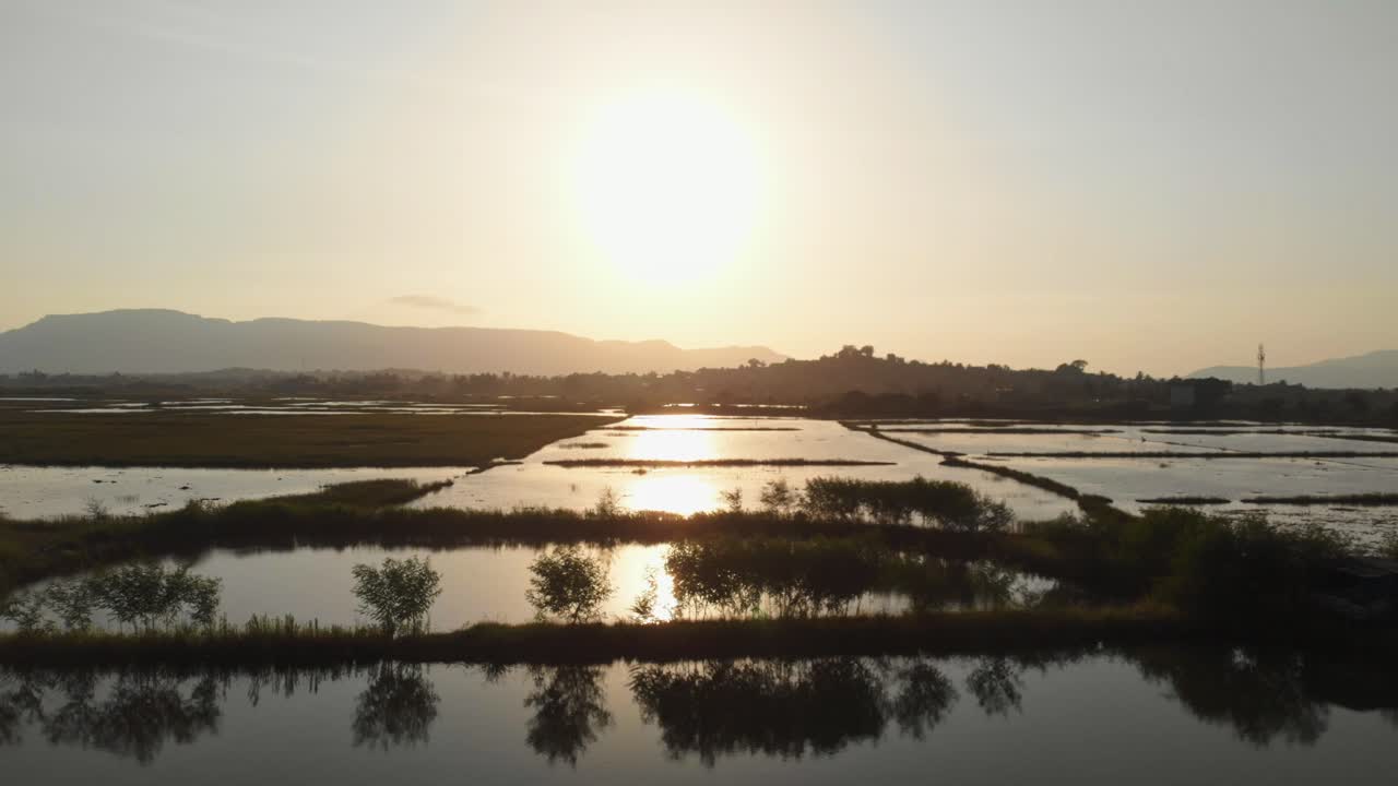 물에 잠긴 인도 논 위로 낮은 드론 슬라이더 샷 - 양어장 일몰
