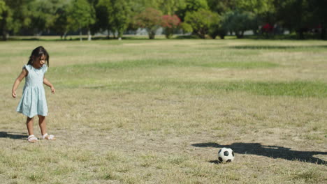 Happy-Asian-little-girl-kicking-ball-to-her-father-outdoors