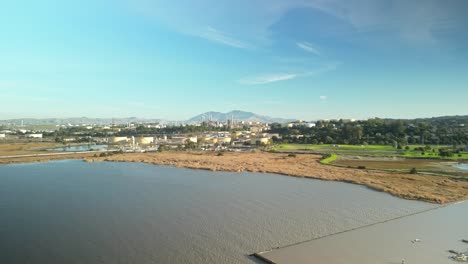 aerial wide tracking left of carquinez strait wetlands and shoreline in martinez, california with industrial plants along horizon