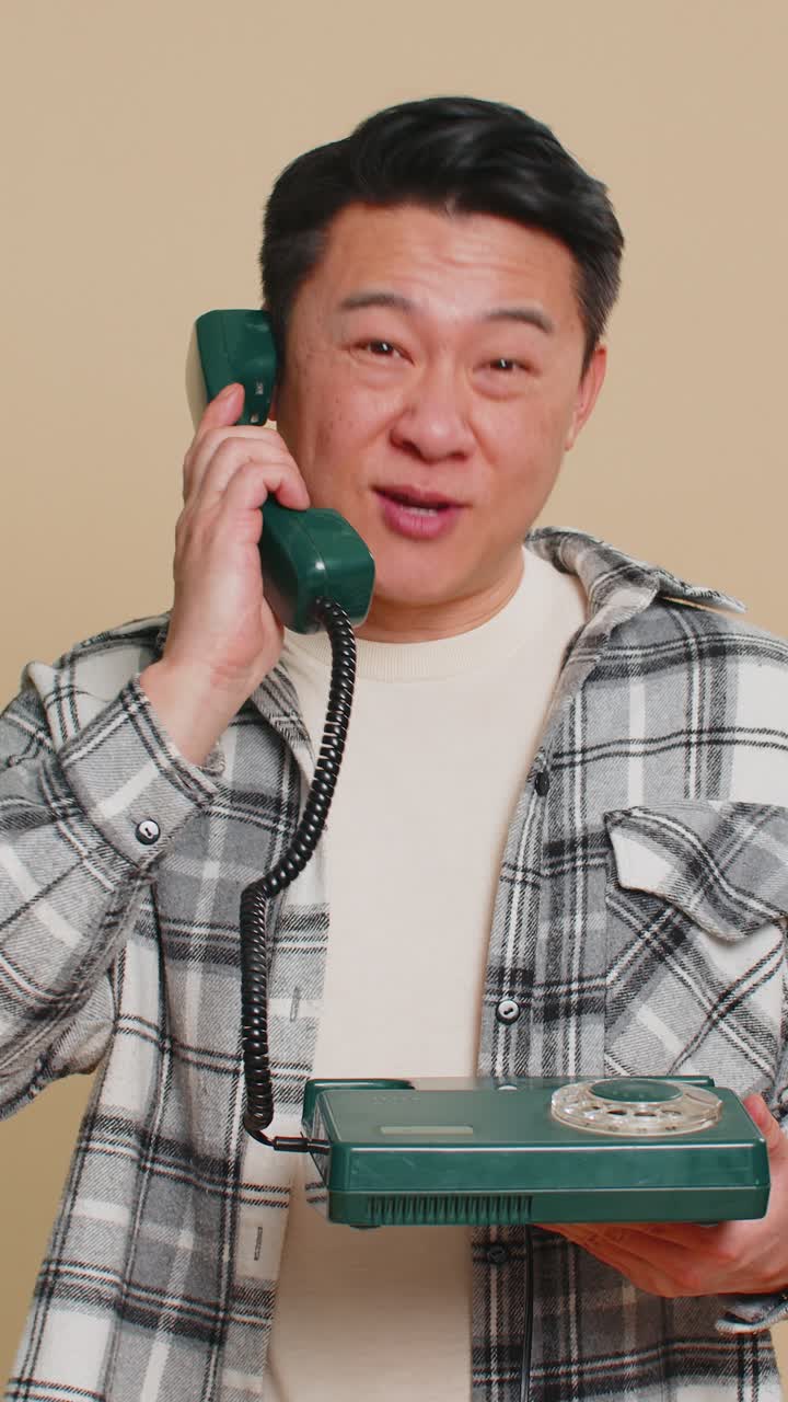Asian man talking on wired landline vintage telephone advertising proposition of conversation