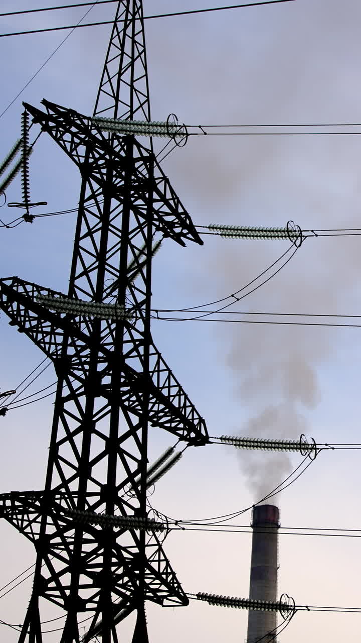 Electricity pylons and smoke from pipes. Wires of high-voltage transmission lines and pipes of industrial plant with thick smoke. Vertical video