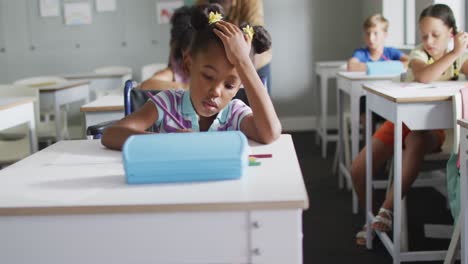 video of focused african american girl sitting at desk in classroom