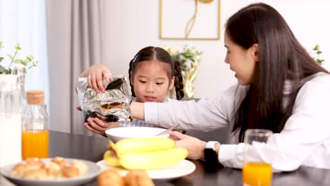 a young girl and her mother share a cheerful breakfast moment as they pour cereal together in a bright, modern dining room with natural light