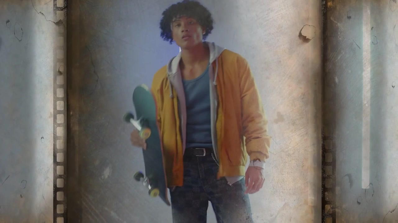 Skater uomo che preme il piede anteriore, solleva la tavola, posando per la moda con un tubo al neon e una pellicola cinematografica.