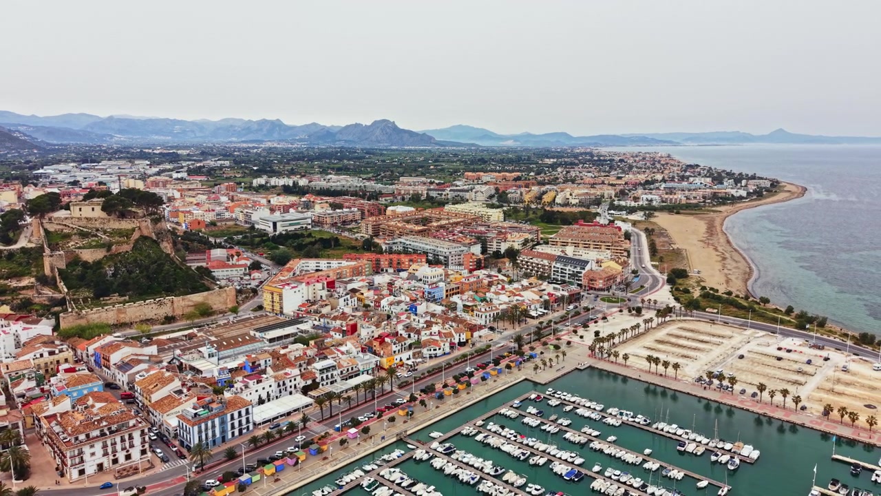 Vista di una città costiera con edifici, barche e montagne in lontananza durante le ore diurne